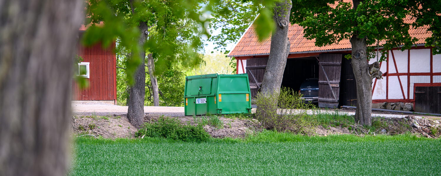 Hyrd grön container står på gårdsplan på landsbygden