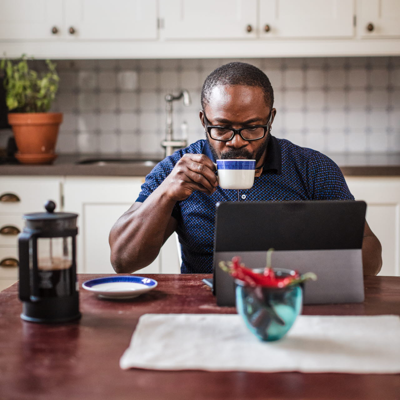 Man dricker kaffe vid datorn i köket