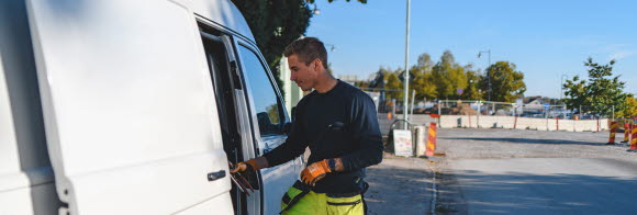 En man i arbetskläder går in i en transportbil med ett verktyg i handen