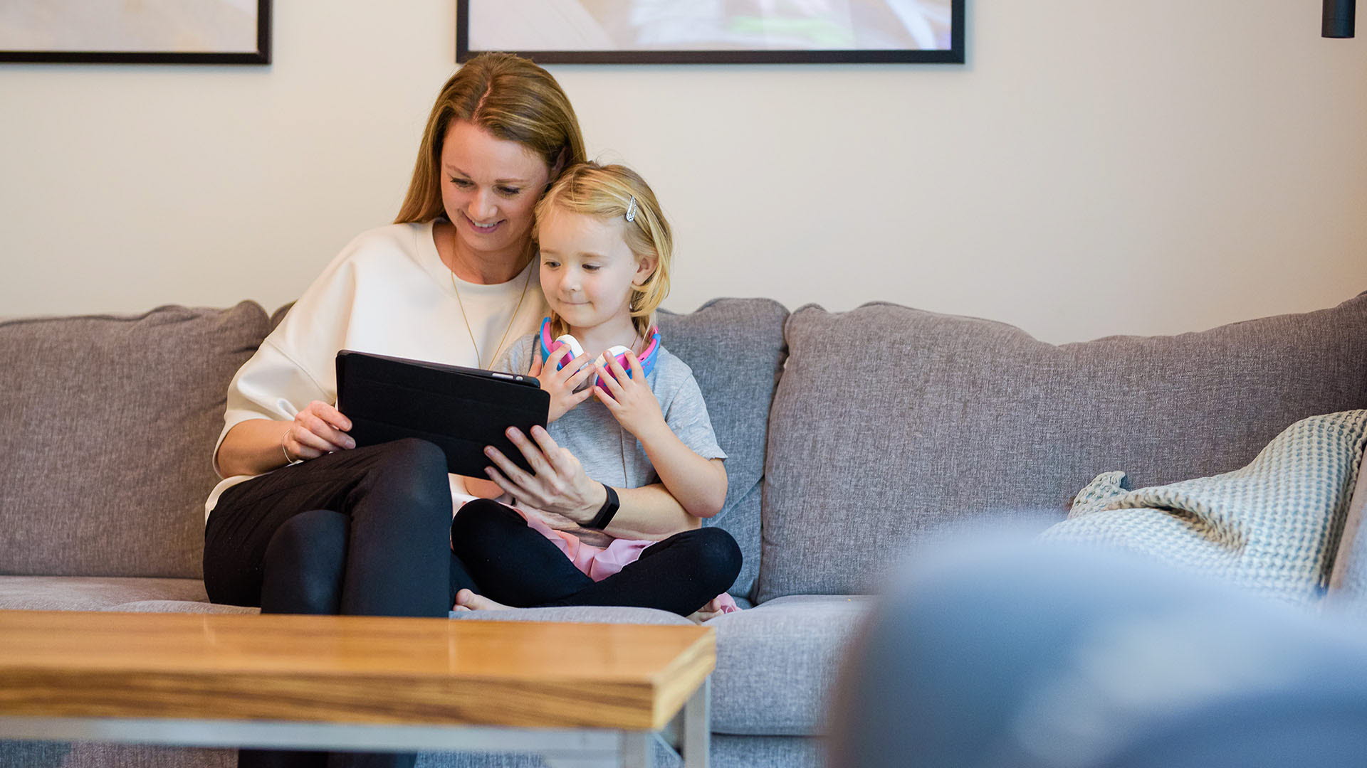 Mamma och dotter sitter i soffan och tittar på en padda tillsammans