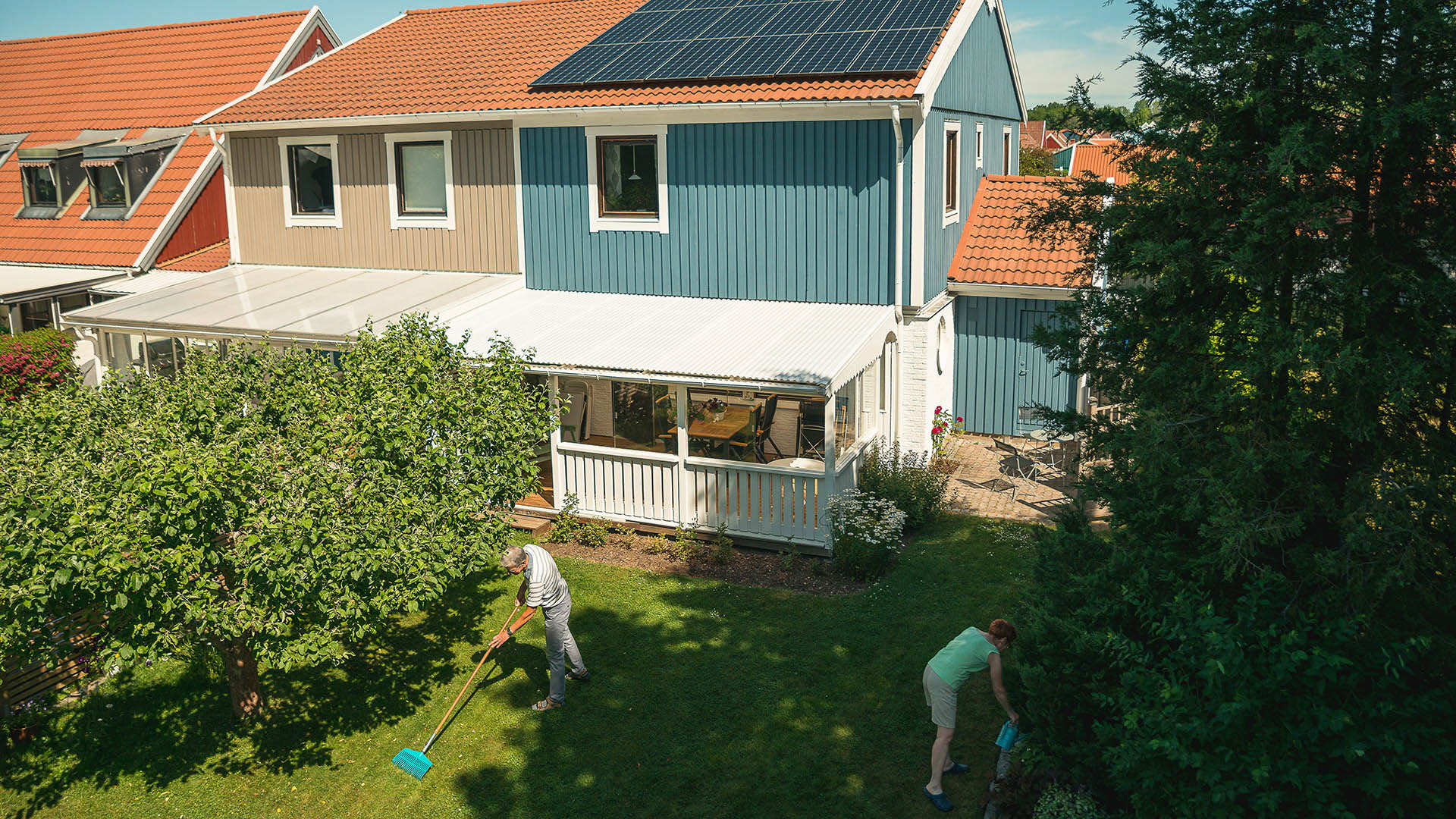 Äldre par arbetar i trädgården. På hustaket syns solceller.