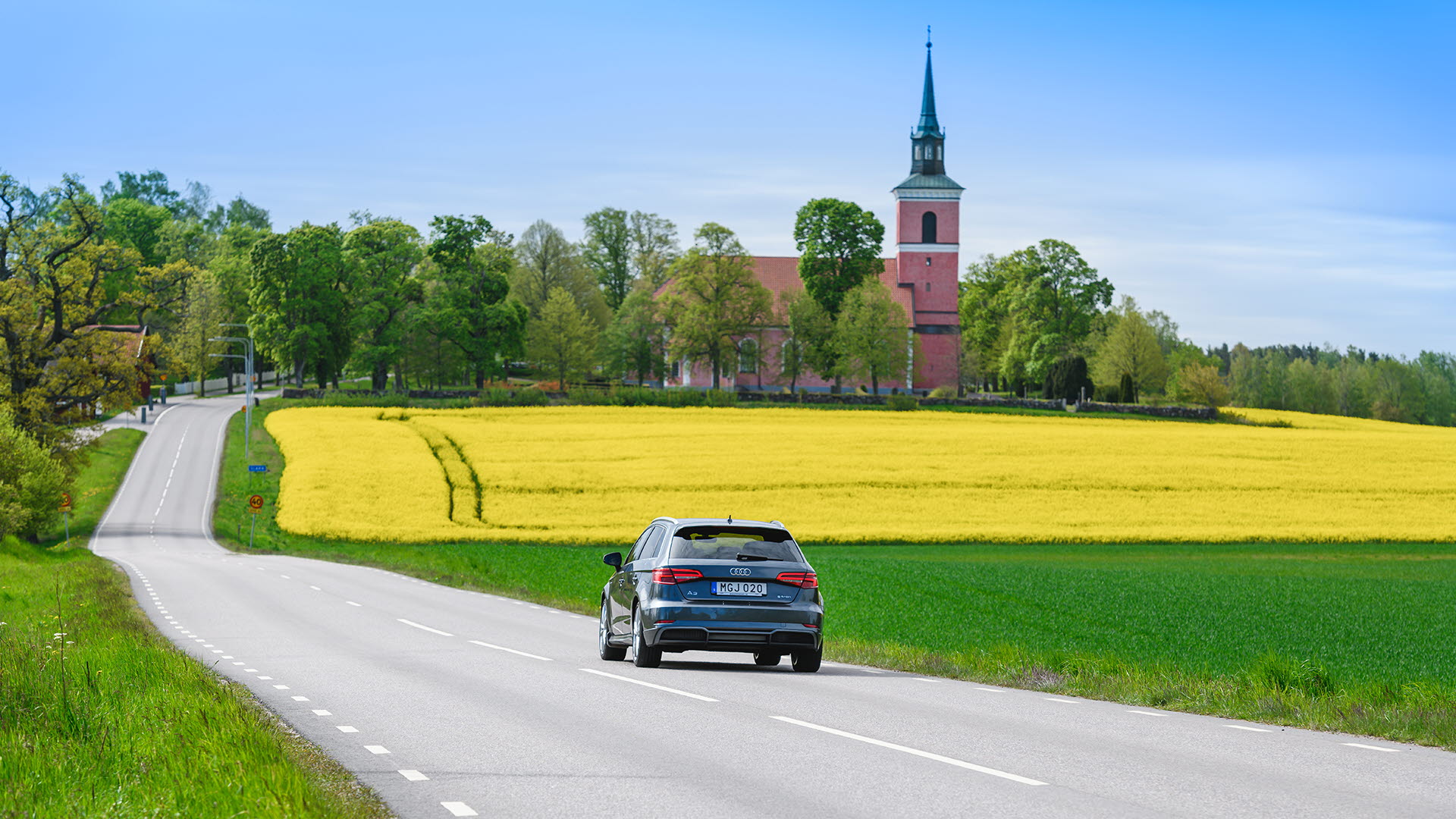 Biogasbil kör på kandsväg med rapsfält och Slaka kyrka i bakgrunden