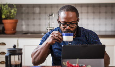 Man dricker kaffe vid datorn i köket