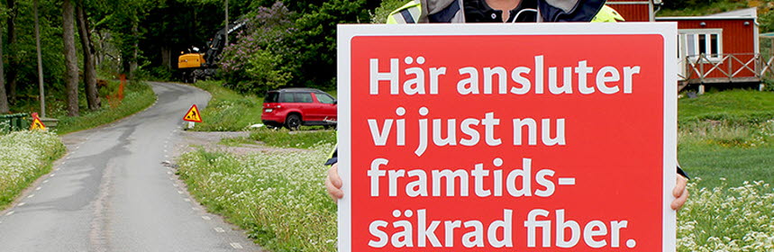 En man håller i skylt där Utsikt Bredband sprider budskapet "Här ansluter vi just nu framtidssäkrad fiber". Foto. 