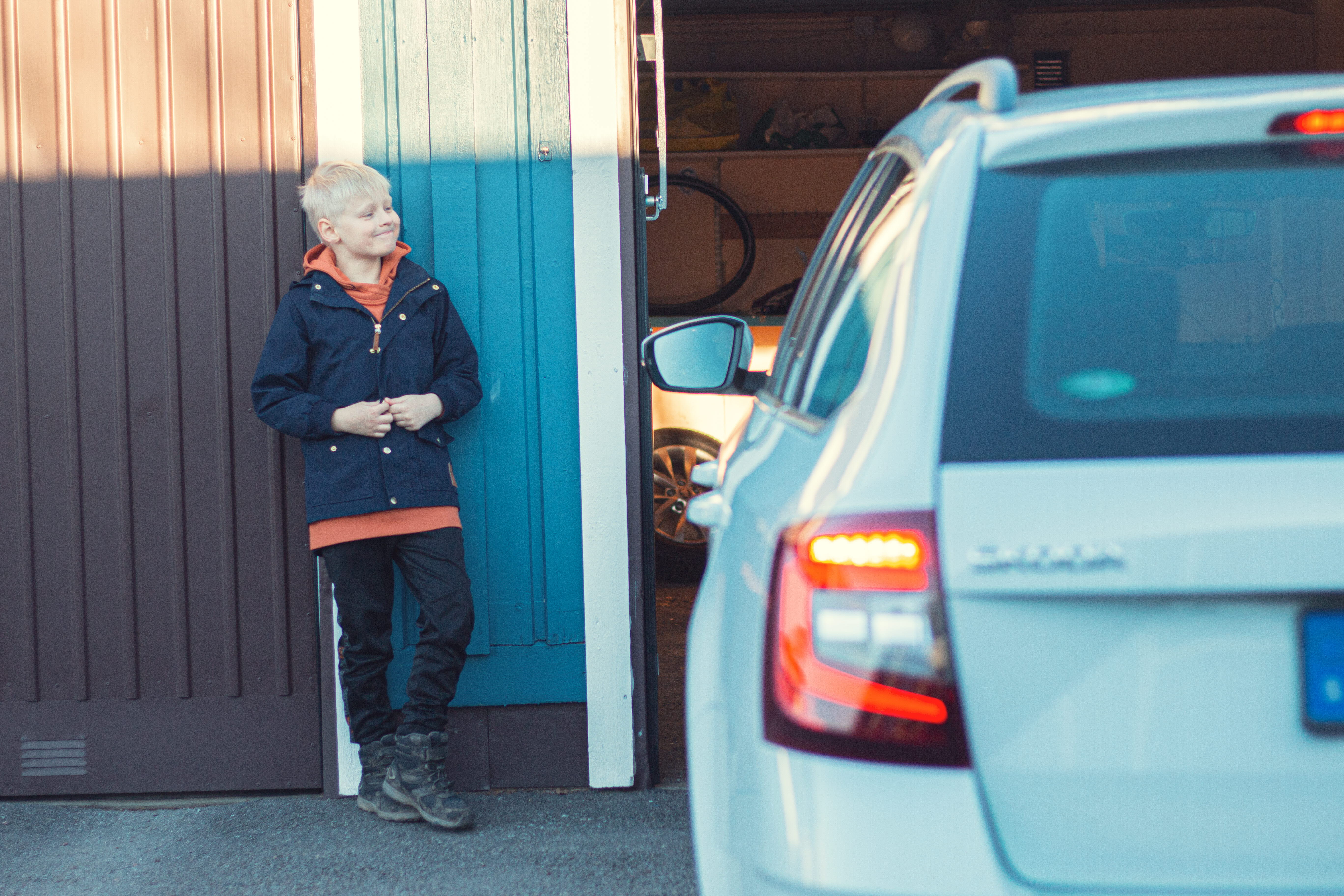 Pojke står vid en vit bil på en garageuppfart (foto)