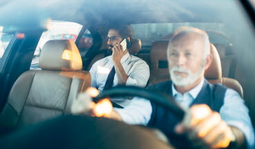 En äldre herre kör taxi med en man som sitter i baksätet. 