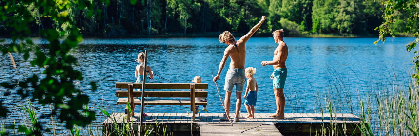 Tre barn och två vuxna står på en badbrygga vid svensk sjö