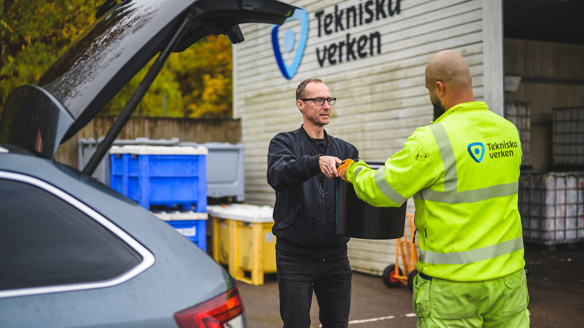 En kund tar emot ett latrinkärl från en medarbetare på återvinningscentralen.