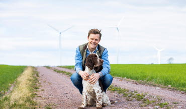 Man med hund framför vindkraftverk (foto)