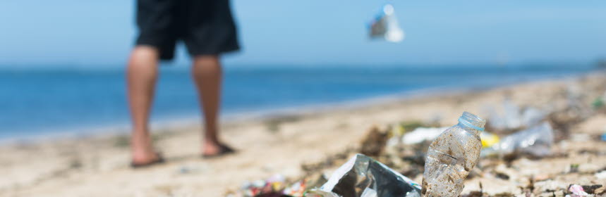 Man slänger skräp på en strand.