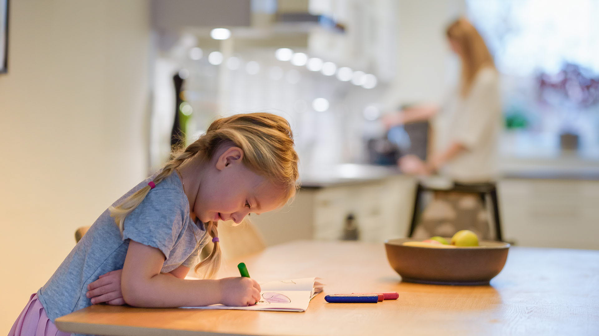 Flickar ritar vid ett bord medan mamma gör kaffe i bakgrunden