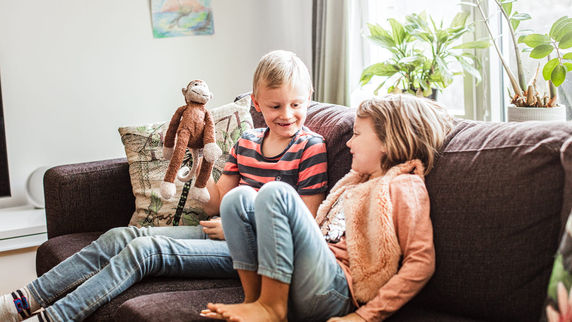 Två barn sitter i en soffa med en mjukdjursapa