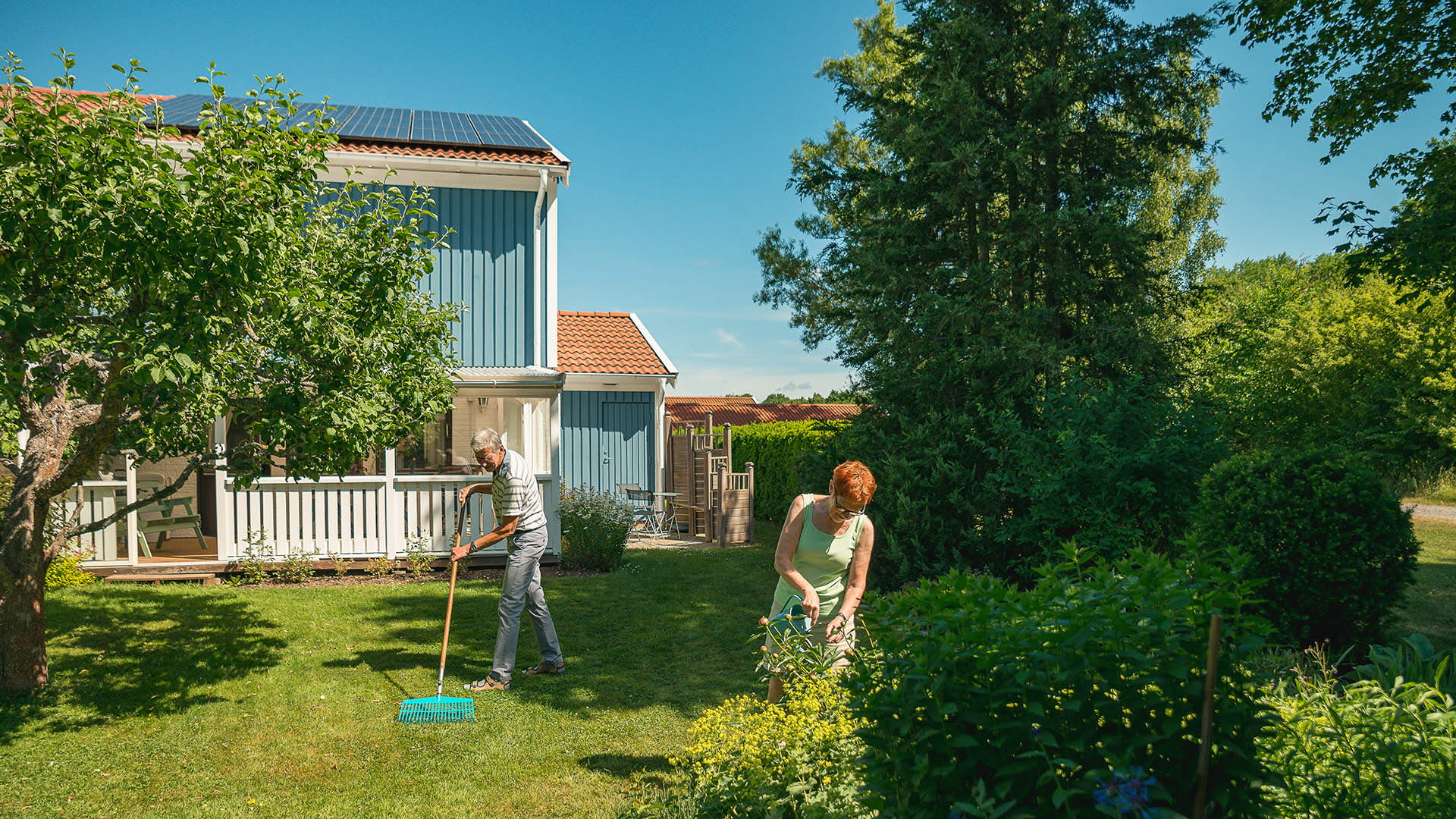 Äldre par arbetar i trädgården. På hustaket syns solceller.