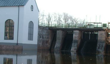 Vattenkraft med pumphus i Flemminge, spegelblankt vatten. Foto. 