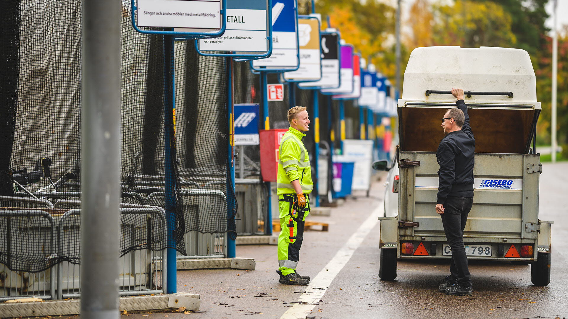 En kund och en medarbetare på återvinningscentralen står och pratar bredvid kundens kärra.