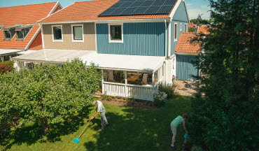 Äldre par arbetar i trädgården. På hustaket syns solceller.