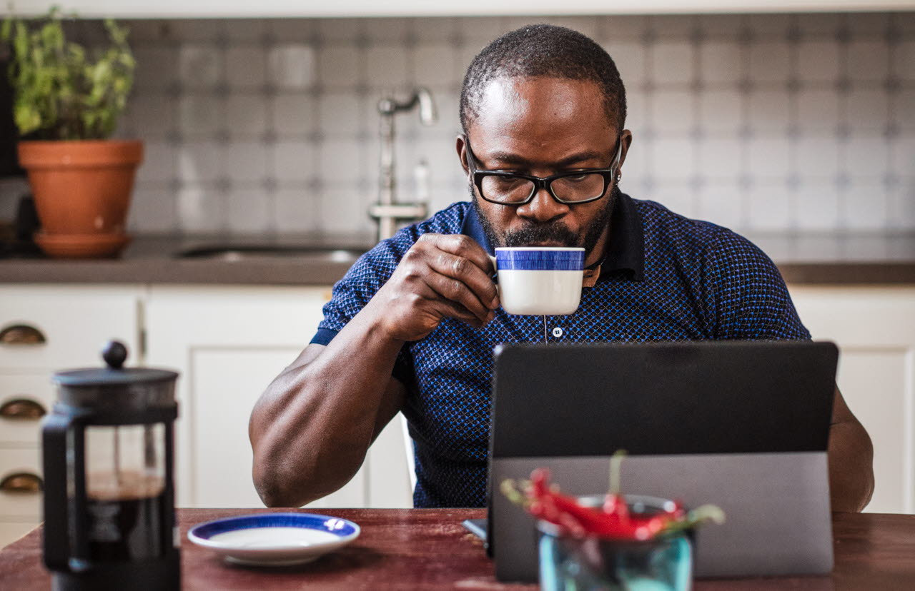 Man dricker kaffe vid datorn i köket