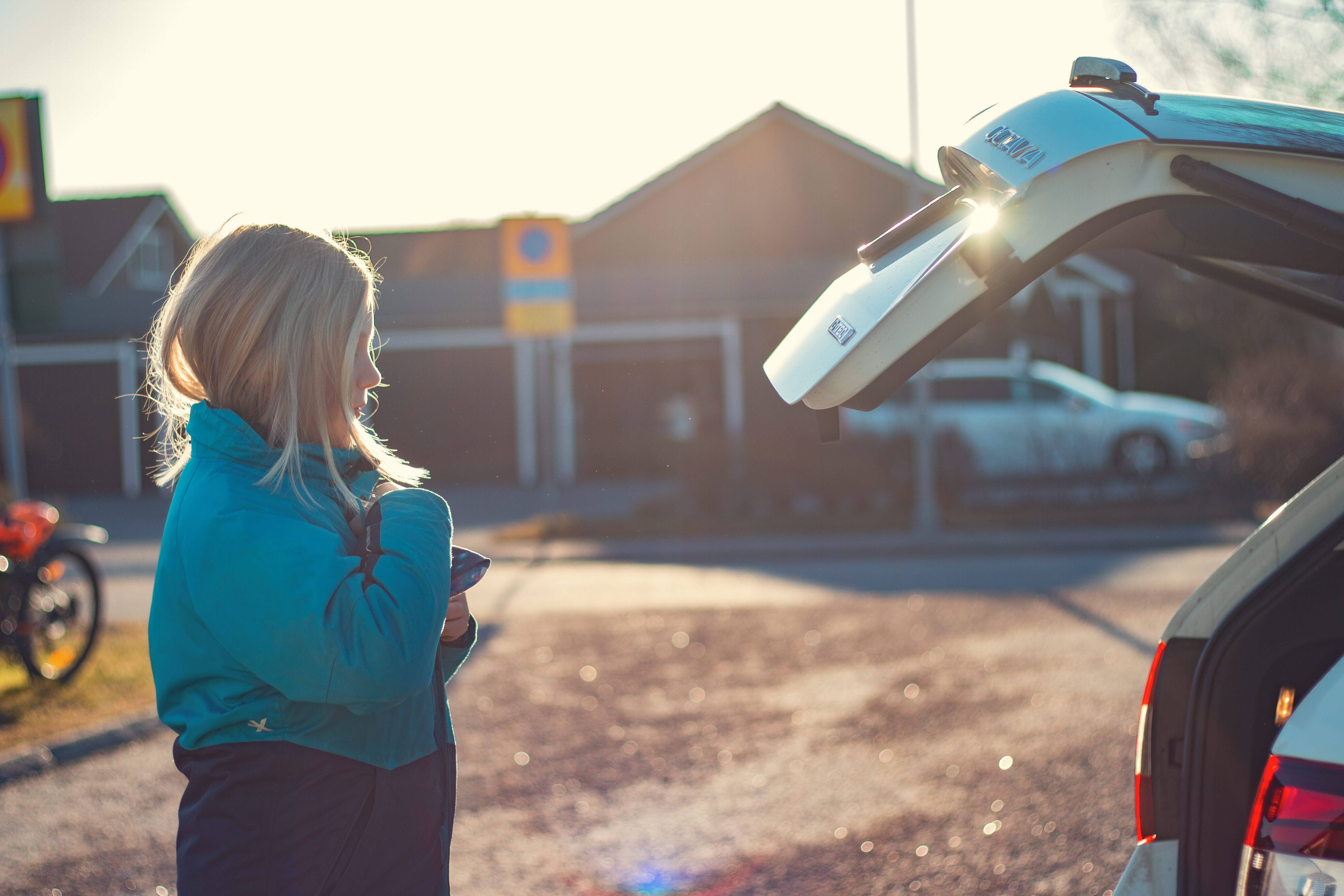 Flicka står vid en vit bil på en garageuppfart (foto)